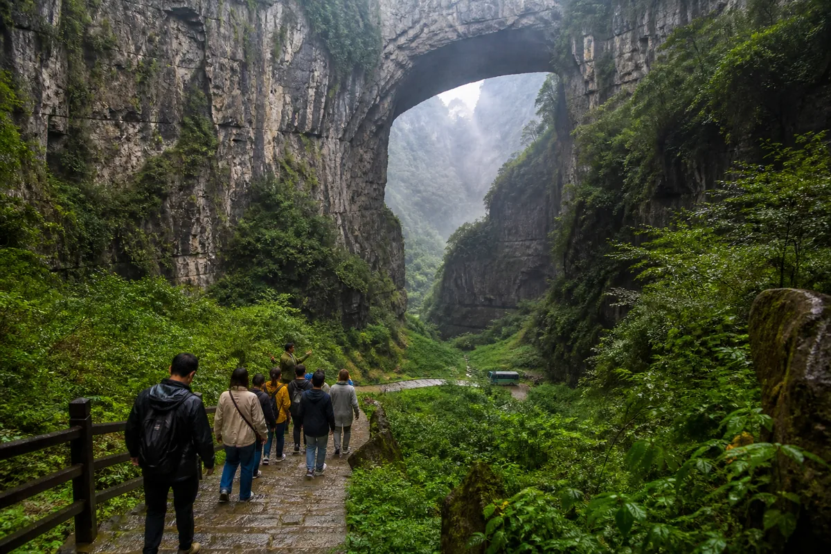 Illustrative small guided group walking beneath a monumental natural bridge in Wulong